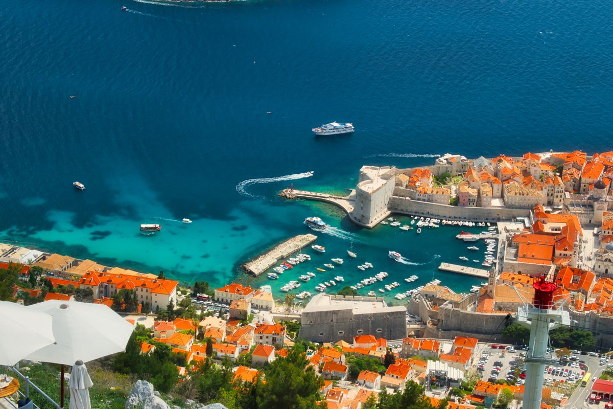A luxury yacht sailing past the ancient city walls of Dubrovnik during a yacht charter Dubrovnik experience in Croatia.